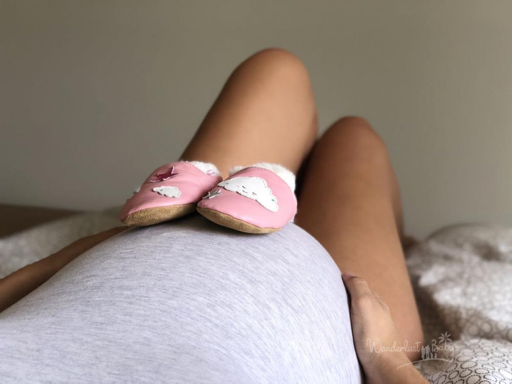 großer Babybauch auf dem zwei rosa Babyschuhe stehen