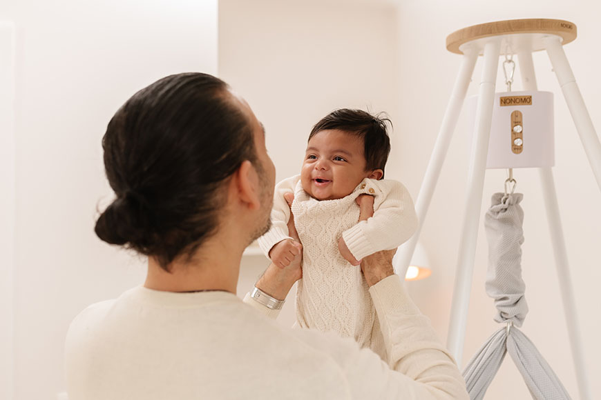 Das Baby wird auf dem Arm gehalten. Im Hintergrund sehen Sie den NONOMO mit Tipi-Ständer und Move-Motor