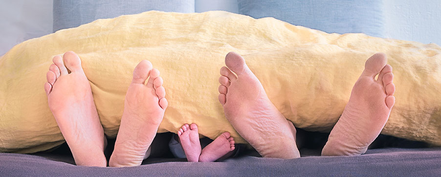 Familie im Bett. Unter einer Decke schauen nur ihre Füße hervor